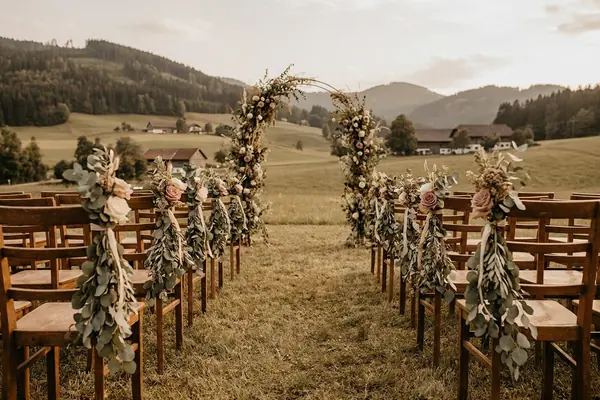 Stuhlreihen mit Grünschmuck vor einem Blumenbogen auf einer Wiese.